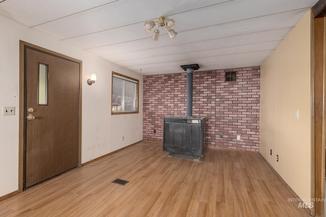 unfurnished living room featuring brick wall, light hardwood / wood-style floors, and a wood stove