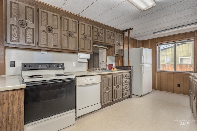 kitchen with white appliances, wooden walls, and sink