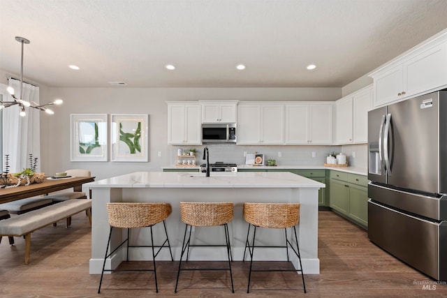 kitchen featuring appliances with stainless steel finishes, hardwood / wood-style flooring, decorative backsplash, and green cabinetry