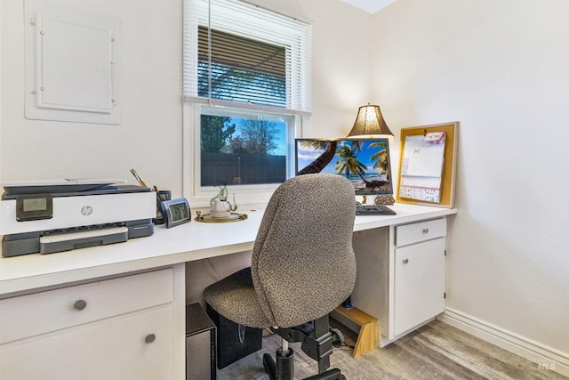 office space with light wood finished floors, built in desk, baseboards, and electric panel