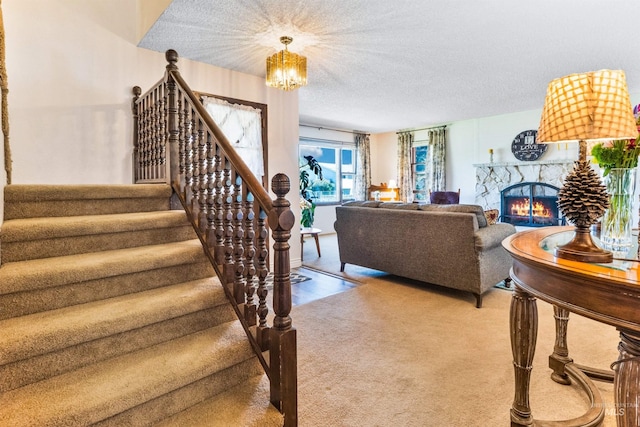 carpeted living room featuring stairway, a chandelier, a stone fireplace, and a textured ceiling