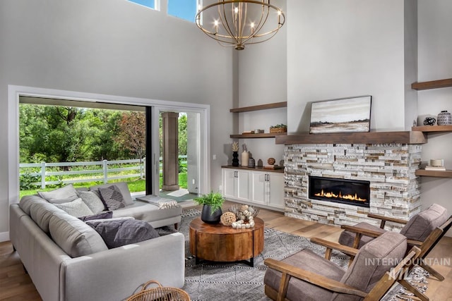 living room featuring a notable chandelier, a high ceiling, a stone fireplace, and light hardwood / wood-style floors