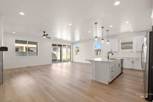 kitchen featuring an island with sink, a sink, open floor plan, stainless steel appliances, and decorative backsplash