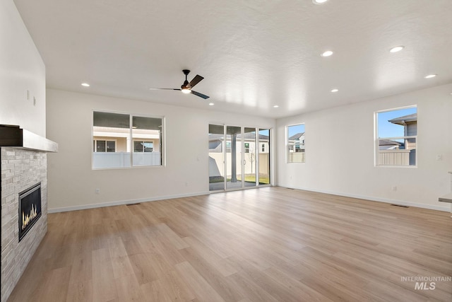 unfurnished living room with a wealth of natural light, a stone fireplace, and light wood-style flooring