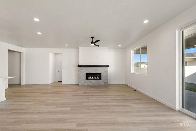 unfurnished living room with baseboards, ceiling fan, a stone fireplace, recessed lighting, and light wood-style flooring