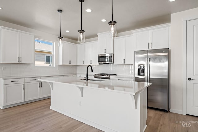 kitchen with a center island with sink, light countertops, white cabinets, stainless steel appliances, and a sink