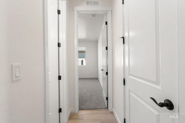 hallway featuring visible vents, light colored carpet, light wood-type flooring, and baseboards