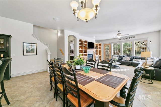 dining room with arched walkways, baseboards, ceiling fan, and a glass covered fireplace