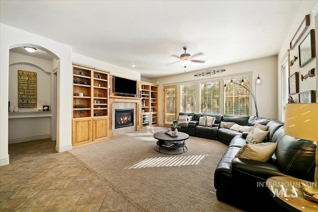 living area with stone finish floor, a fireplace, arched walkways, a ceiling fan, and baseboards