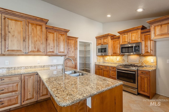 kitchen with stainless steel appliances, a peninsula, a sink, brown cabinets, and tasteful backsplash