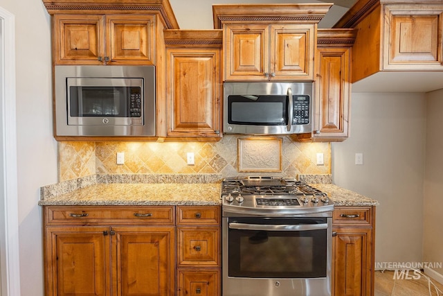 kitchen featuring light stone counters, decorative backsplash, appliances with stainless steel finishes, brown cabinetry, and baseboards