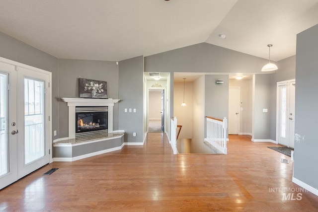 unfurnished living room with french doors, lofted ceiling, visible vents, a glass covered fireplace, and wood finished floors