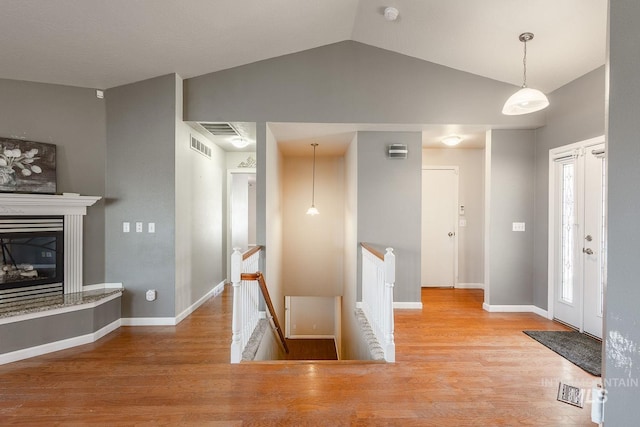 interior space featuring a glass covered fireplace, lofted ceiling, baseboards, and wood finished floors