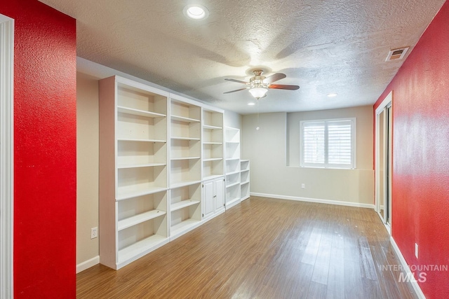 empty room with a textured ceiling, wood finished floors, visible vents, and baseboards