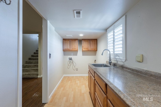 kitchen featuring light wood-style flooring, a sink, visible vents, baseboards, and brown cabinets