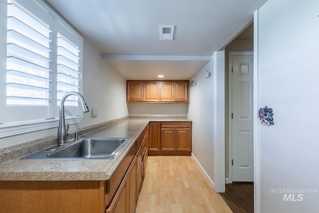 kitchen featuring brown cabinets, visible vents, a sink, light wood-type flooring, and baseboards