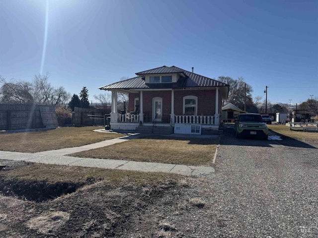 bungalow featuring fence, covered porch, a front lawn, brick siding, and metal roof