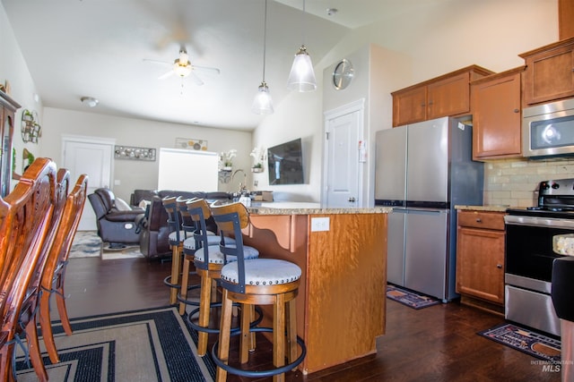 kitchen featuring vaulted ceiling, a center island with sink, appliances with stainless steel finishes, dark wood-type flooring, and ceiling fan