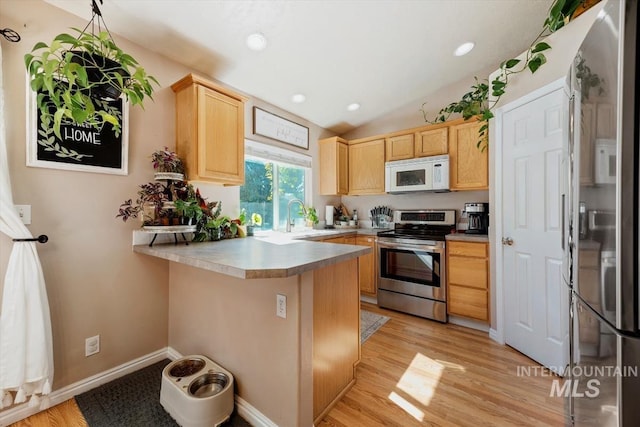 kitchen with a peninsula, stainless steel appliances, light brown cabinetry, light wood-type flooring, and a sink