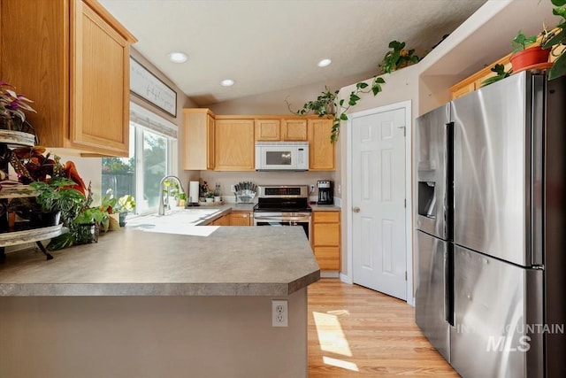 kitchen featuring lofted ceiling, appliances with stainless steel finishes, light wood finished floors, and light brown cabinets