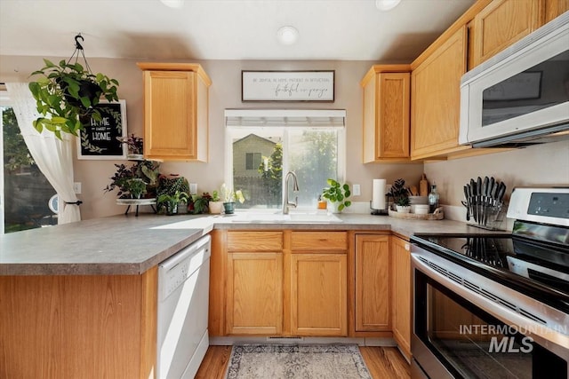 kitchen featuring light wood-style flooring, a peninsula, white appliances, a sink, and light countertops