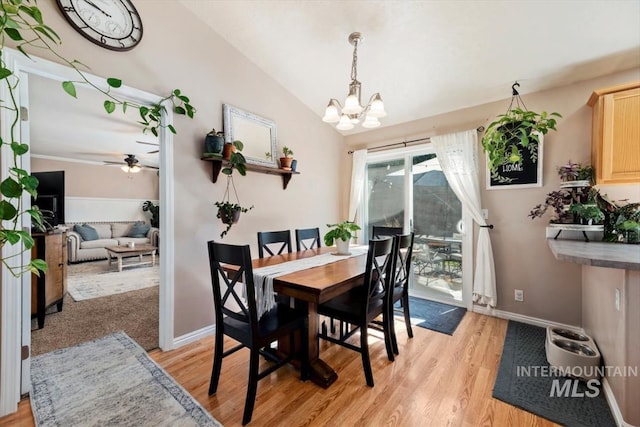 dining room featuring light wood-type flooring, baseboards, vaulted ceiling, and ceiling fan with notable chandelier