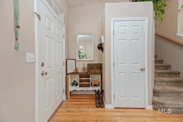 foyer entrance with light wood-style floors, baseboards, and stairway