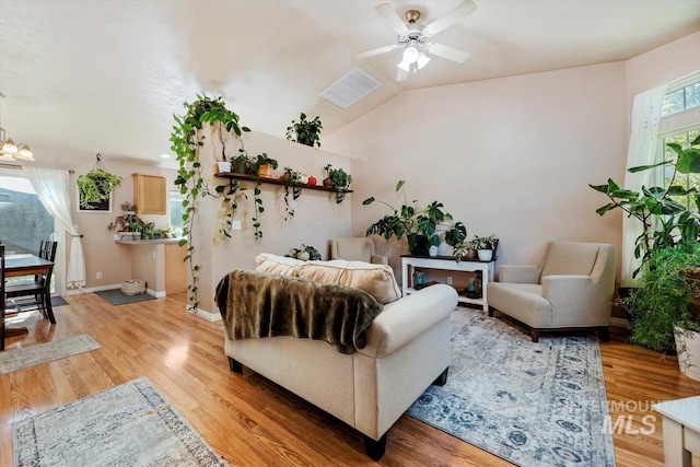 living area with vaulted ceiling, ceiling fan with notable chandelier, baseboards, and light wood-style floors