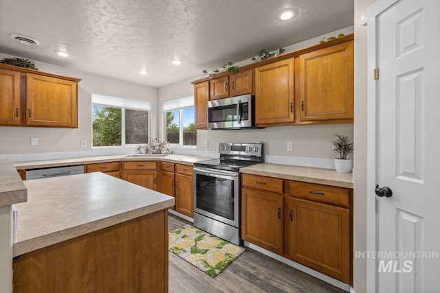 12339 W Foxhaven St, Star, ID 83669 - kitchen featuring stainless steel appliances, wood finished floors, brown cabinetry, a textured ceiling, and light countertops