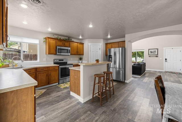 12339 W Foxhaven St, Star, ID 83669 - kitchen featuring stainless steel appliances, arched walkways, brown cabinetry, dark wood finished floors, and a center island