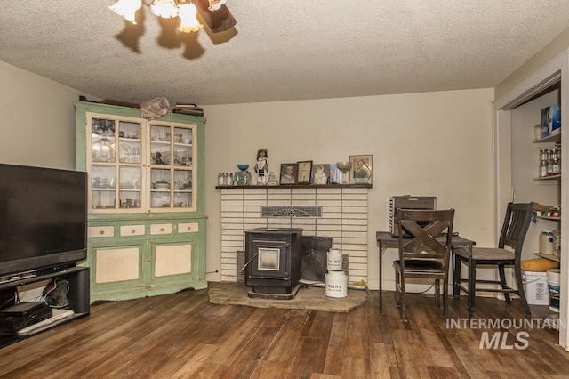 living room with ceiling fan, a wood stove, a textured ceiling, and wood finished floors