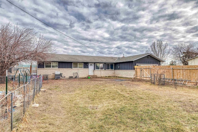 back of house with brick siding, board and batten siding, fence, and a lawn