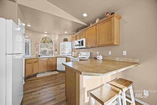 16702 Frisco Ave, Caldwell, ID 83607 - kitchen featuring white appliances, a peninsula, dark wood-type flooring, a textured ceiling, and vaulted ceiling
