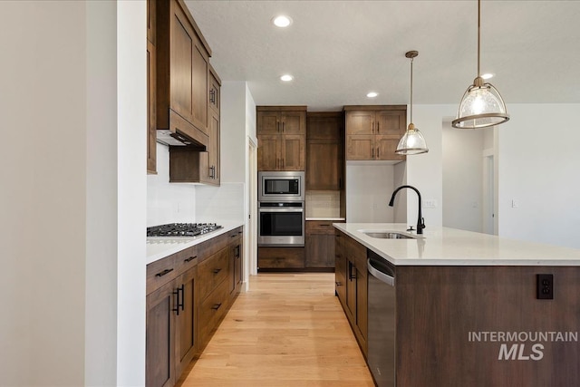 kitchen featuring stainless steel appliances, light hardwood / wood-style flooring, decorative light fixtures, a kitchen island with sink, and sink