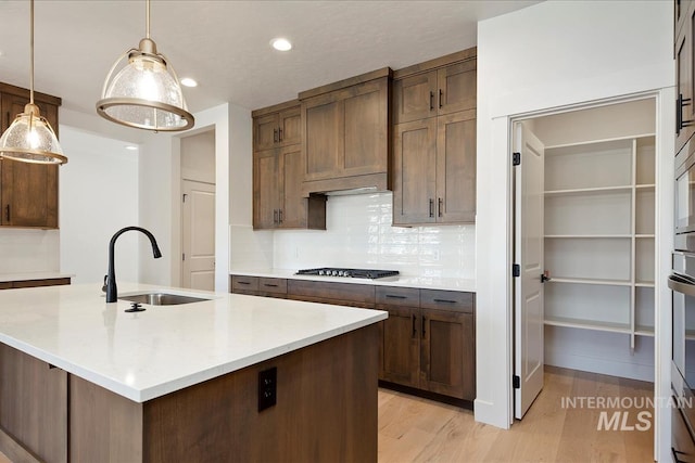 kitchen with decorative backsplash, light hardwood / wood-style floors, decorative light fixtures, a center island with sink, and sink