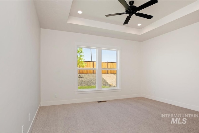 unfurnished room with light colored carpet, ceiling fan, and a raised ceiling