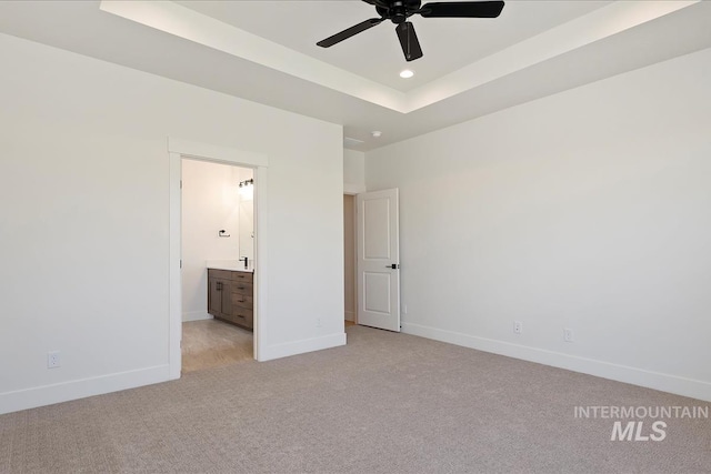 unfurnished bedroom with a raised ceiling, ensuite bath, ceiling fan, and light colored carpet