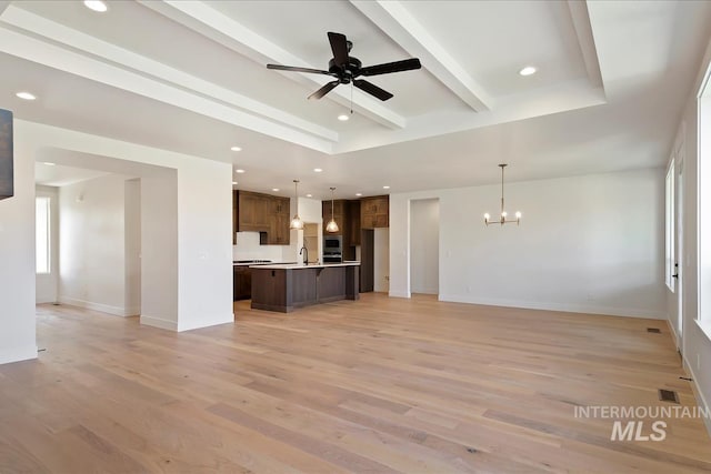 unfurnished living room featuring ceiling fan with notable chandelier, beam ceiling, light hardwood / wood-style flooring, and sink