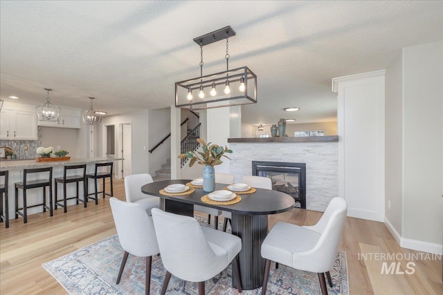 1499 E Sicily St, Meridian, ID 83642 - dining space with stairway, light wood-style flooring, a fireplace, a textured ceiling, and a chandelier