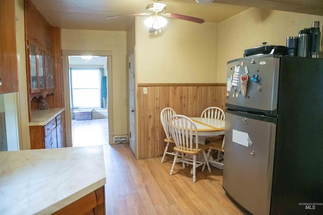 kitchen with light hardwood / wood-style flooring, stainless steel fridge, wood walls, and ceiling fan