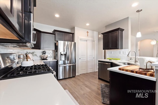 kitchen with sink, light hardwood / wood-style flooring, stainless steel appliances, tasteful backsplash, and decorative light fixtures