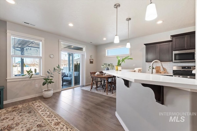 kitchen with dark brown cabinets, hanging light fixtures, a kitchen breakfast bar, stainless steel appliances, and backsplash