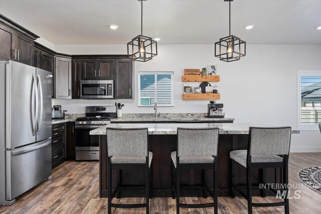 kitchen featuring appliances with stainless steel finishes, light stone countertops, dark hardwood / wood-style flooring, pendant lighting, and a center island