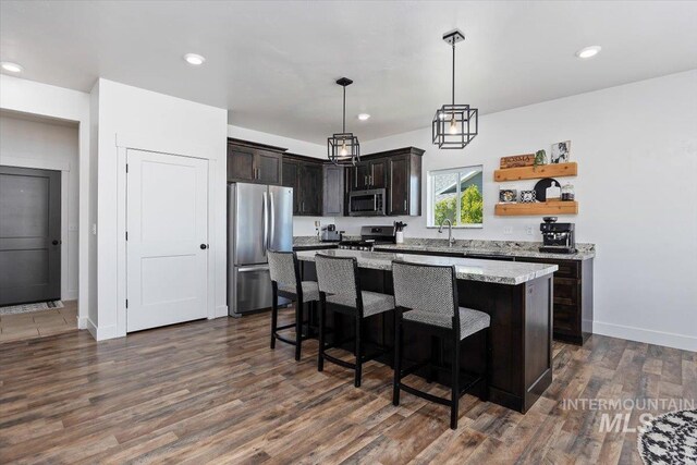 kitchen with light stone counters, dark brown cabinetry, dark wood-type flooring, stainless steel appliances, and a center island