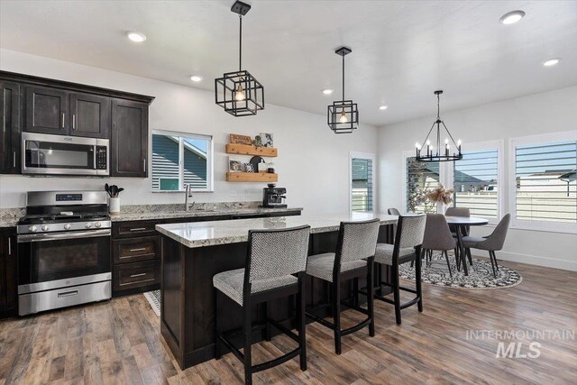 kitchen with a kitchen island, dark wood-type flooring, stainless steel appliances, a kitchen breakfast bar, and a notable chandelier