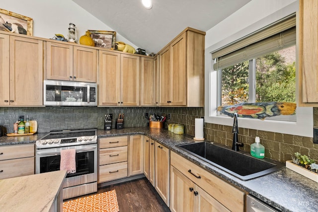 kitchen featuring vaulted ceiling, appliances with stainless steel finishes, light brown cabinetry, sink, and dark wood-type flooring