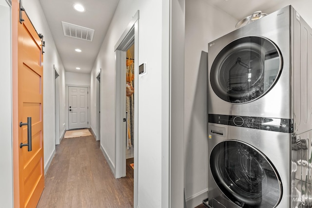 clothes washing area with stacked washer / dryer, a barn door, and hardwood / wood-style floors