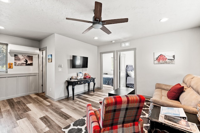 living room featuring ceiling fan, an AC wall unit, a textured ceiling, and light hardwood / wood-style floors