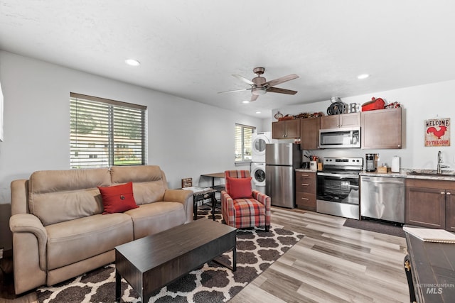 living room featuring stacked washer and dryer, sink, a textured ceiling, ceiling fan, and light hardwood / wood-style floors