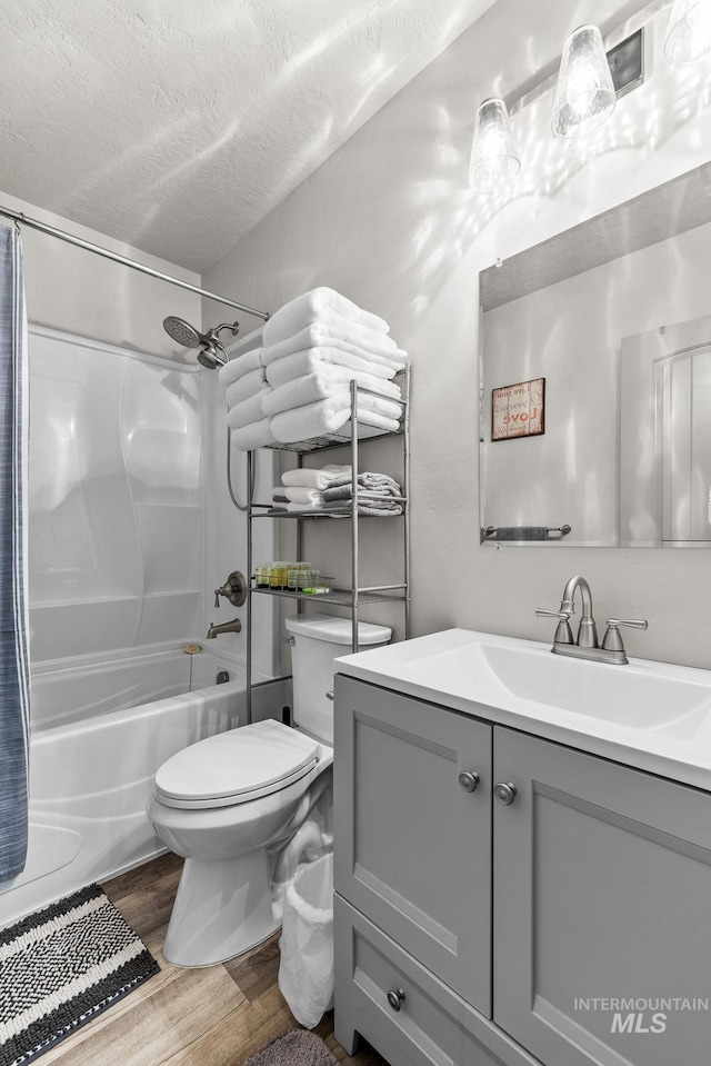 full bathroom with hardwood / wood-style floors, shower / bath combination with curtain, vanity, toilet, and a textured ceiling